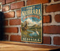 A vintage-style sign for the Fort Niobrara National Wildlife Refuge in Nebraska, featuring an illustration of a ram and a white bird in a grassy field with a river.