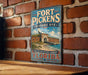 A vintage-style sign for the Fort Pickens Historic Site in Florida, featuring a brick wall and a seashore scene.