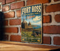 A vintage-style metal sign for Fort Ross State Historic Park in California, featuring a barn and a cannon, mounted on a brick wall.