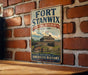 A vintage-style metal sign for Fort Stanwix, a National Monument in New York, featuring an illustration of the fort and its surroundings.