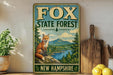 A vintage metal sign for the Fox State Forest in New Hampshire, featuring an illustration of a fox in a forest setting.