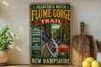 a vintage-style sign for the Franconia Notch Flume Gorge Trail in New Hampshire, with a scenic mountain landscape and a wooden board.