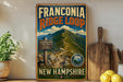 A vintage-style metal sign for the Franconia Ridge Loop Trail in New Hampshire, featuring a mountain landscape with a trail leading up to a peak.