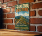 A vintage trail sign for the Franconia Ridge Trail in Massachusetts, featuring a mountain landscape with a winding path.