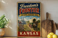 A vintage-style metal sign advertising the "Freedom's Frontier National Heritage Area" in Kansas, featuring an illustration of a steamboat and a covered wagon.