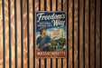 A vintage metal sign with the text "Freedom's Way" and "National Heritage Area" is displayed on a wooden wall.