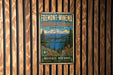 a vintage metal sign with a mountain landscape and a lake, mounted on a wooden wall.