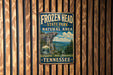 A vintage metal sign for Frozen Head State Park and the Natural Area in Tennessee, featuring a scenic mountain landscape.