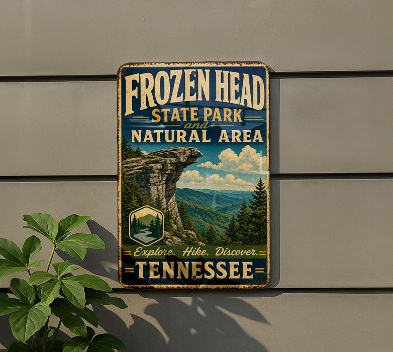 A vintage-style metal sign for Frozen Head State Park and Natural Area in Tennessee, featuring a scenic mountain landscape and the text "FROZEN HEAD STATE PARK AND NATURAL AREA EXPLORE. HIK. DISCOVER. TENNESSEE".