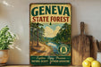 a vintage-style metal sign for the Geneva State Forest, with a scenic illustration of a forest and a river. The sign is displayed on a shelf next to a wooden cutting board and a potted plant.