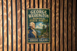 A vintage metal sign with the text "GEORGE WASHINGTON MEMORIAL STATE FOREST RHODE ISLAND" and an illustration of George Washington, the first President of the United States, is displayed on a wooden wall.