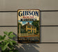 A vintage metal sign for the Gibson House Museum in Massachusetts, featuring an illustration of a yellow house with a white picket fence and a chimney.