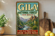 A vintage-style metal sign advertising Gila National Forest in New Mexico, featuring a scenic mountain landscape with a river and desert vegetation.