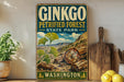 A vintage-style metal sign for Ginkgo Petrified Forest State Park in Washington, featuring an illustration of ginkgo leaves and logs against a mountainous landscape.