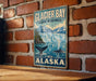 A vintage metal sign for Glacier Bay Marine Wilderness in Alaska, featuring a scenic image of a waterfall and a whale.