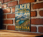 A vintage metal sign with the text "Glacier Country Cultural Landscape" and "Montana" is displayed on a brick wall.