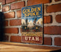 A vintage-style sign for Golden Spike National Historical Park in Utah, featuring an illustration of a train and the text "Golden Spike National Historical Park" and "Where the Nation was United".