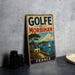 A vintage-style metal sign with the text "GOLFÉ DU MORBIHAN FRANCE" is displayed on a gray concrete surface, accompanied by a small white dish and a stack of black camera lenses.