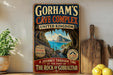 A vintage-style metal sign advertising the Gorham's Cave Complex in United Kingdom, featuring a scenic image of the cave entrance and a description of the cave exploration.