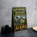 A vintage-style sign for Governor's mansion in Alaska, featuring a large illustration of the mansion and the state's flag.