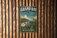 A vintage-style metal sign for the Grand Bay National Estuarine Research Reserve in Mississippi, featuring an illustration of a bird, flowers, and a river.