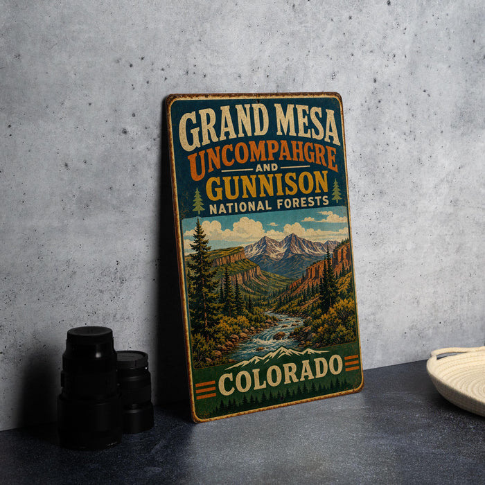 A vintage-style metal sign for Grand Mesa, Colorado, featuring a scenic mountain landscape with a river and pine trees.