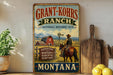 a vintage-style sign for Grant-Kohrs Ranch, which is a National Historic Site in Montana. The sign depicts a cowboy riding a horse in front of a red barn, with mountains in the background. The sign also includes the text "Grant-Kohrs Ranch" and "Montana", indicating the location and name of the ranch.