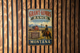 A vintage metal sign for Grant-Kohrs Ranch, a National Historic Site in Montana, featuring a cowboy on horseback and a barn in the background.