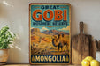 A vintage-style metal sign advertising the Great Gobi Biosphere Reserve in Mongolia, featuring illustrations of various animals such as a camel, gazelle, and antelope in a desert landscape.