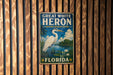 A vintage-style metal sign for the Great White Heron National Wildlife Refuge in Florida, featuring a large heron standing in a pond surrounded by lush vegetation.