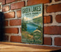 A vintage-style metal sign for Green Lakes State Park in New York, featuring a scenic image of the lake surrounded by trees and mountains.