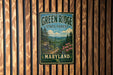 A vintage-style metal sign for the Green Ridge State Forest in Maryland, featuring a scenic landscape with pine trees, mountains, and pink flowers.