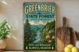 A vintage-style sign for the Greenbrier State Forest in West Virginia, featuring a scenic mountain landscape with a river and pine trees.