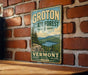 A vintage-style metal sign for Groton State Forest in Vermont, featuring a scenic landscape with pine trees and a lake.