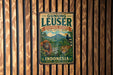 A vintage-style metal sign with a forest scene and wildlife, including an orangutan, tiger, and bird, is displayed on a wooden wall.