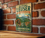 A vintage-style metal sign with text and illustrations of an orangutan, tiger, and lush green forest, mounted on a brick wall.