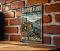 A vintage metal sign for Harpers Ferry National Historical Park, featuring a scenic illustration of the park and its surroundings.