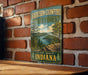 A vintage metal sign for Harrison-Crawford State Forest, featuring a scenic landscape with a river and trees, is displayed on a brick wall.