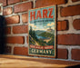 A vintage metal sign for Harzbrüsseger Land Park in Germany, featuring a scenic landscape with a castle and a river.