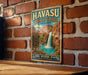 A vintage-style metal sign for Havasu Falls Trail in Arizona, featuring a waterfall and mountains in the background.