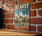 A vintage metal sign with the text "HEART CASTLE CALIFORNIA" and an illustration of a castle surrounded by palm trees and a fountain.