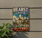 A vintage-style metal sign with the text "HEARST CASTLE CALIFORNIA" and an illustration of a castle surrounded by palm trees and a fountain.