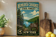 A vintage-style metal sign for Hemlock-Canadice State Forest in New York, featuring a scenic landscape with pine trees, a lake, and mountains.