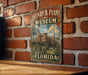 A vintage-style metal sign for the Henry B. Plant Museum in Florida, featuring an illustration of a historic building with palm trees.