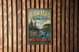 A vintage metal sign for the Hiawatha National Forest in Michigan, featuring a scenic illustration of a lake surrounded by pine trees and mountains.