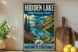 A vintage-style sign for "Hidden Lake" in the Northwest Territories, featuring a scenic mountain landscape with a lake and pine trees.