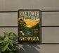 A vintage-style metal sign for the Hightower Forest in Georgia, featuring a scenic landscape with pine trees, a river, and a sunset.