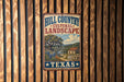 A vintage-style metal sign with the text "HILL COUNTRY CULTURAL LANDSCAPE TEXAS" displayed on a wooden fence.