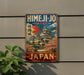 A vintage-style metal sign with a picture of a Japanese castle, surrounded by cherry blossoms, is mounted on a wall.