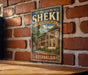 A vintage-style sign for the Historic Centre of Sheki, featuring an illustration of a palace and the text "SHEKI WITH THE KHAN'S PALACE" and "AZERBaijan".